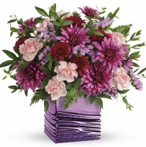 Lavender roses, light pink miniature carnations, burgundy cushion spray chrysanthemums, purple cushion spray chrysanthemums and lavender sinuata statice are arranged with huckleberry and parvifolia eucalyptus. Delivered in a Liquid Lavender cube.